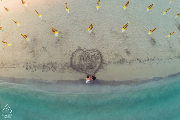 Siracusa beach reveals a unique pattern of closed umbrellas and a loving couple making a heart in the sand