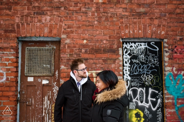 Quebec couple stands in a gritty urban alleyway in winter jackets 