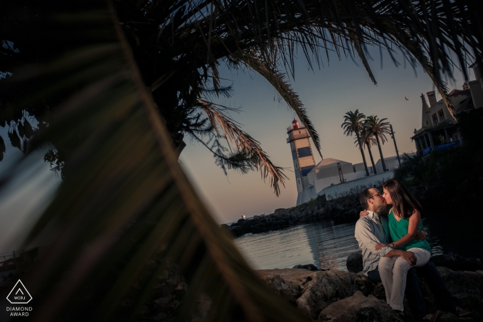 The Lisbon engaged couple sits on the rocks beneath a palm tree