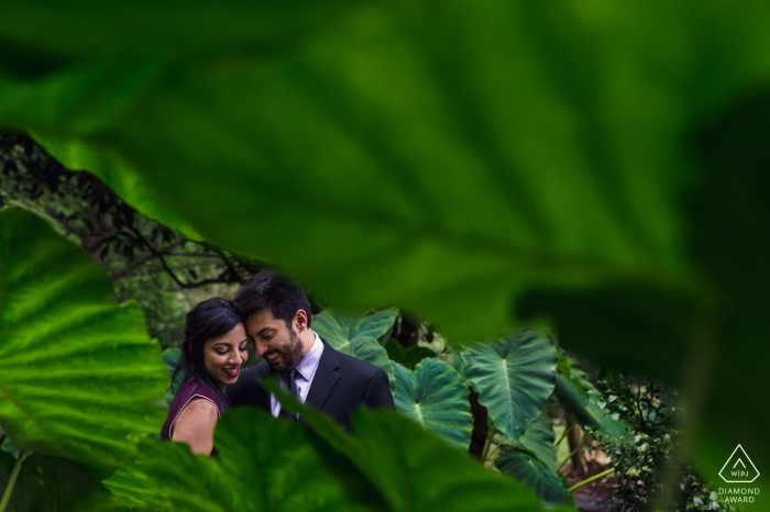 A lovestruck couple embrace in the lush, green jungle scene of Atlanta, Georgia, with a large leaf framing their embrace