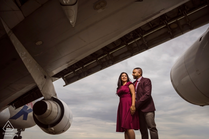 A London couple standing close at the airport under the wing of an aircraft during engagement shoot