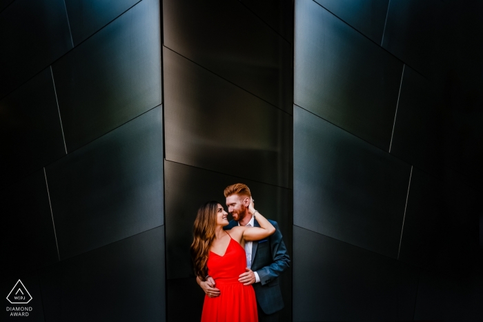 Kalifornisches Foto vor der Hochzeit eines Paares, das sich in industrieller Umgebung mit ihrem roten Kleid umarmt