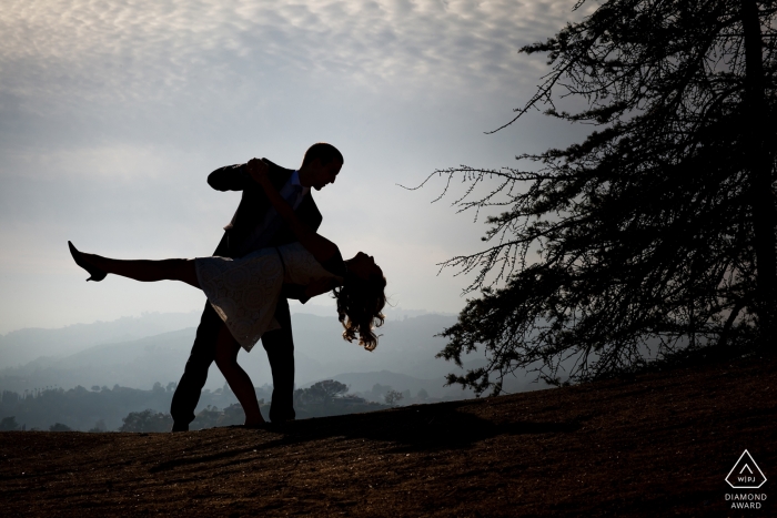 A playful California couple dancing and dipping against a pale sky