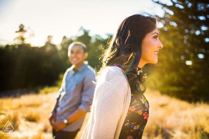 A CA engagement photo captures the couple smiling in a dry grass field, with the warm glow of sunlight adding a romantic atmosphere to the scene