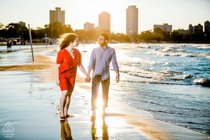 Ein verlobtes Paar aus Illinois geht auf reflektierendem Sand in der Nähe der Strandskyline spazieren