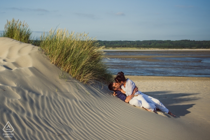 Un couple de fiancés s'embrasse sur une dune de sable balayée par le vent avec des herbes marines