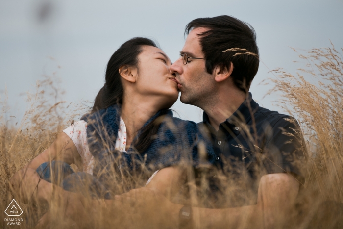 Photo by: <a href="https://www.wpja.com/photos/diamond-award-top-wedding-engagement-photographer/2427071">Ronnie Szeto - Tseung Kwan O Nordsee, Germany engagement portrait of a couple sitting in tall wispy Grass while kissing