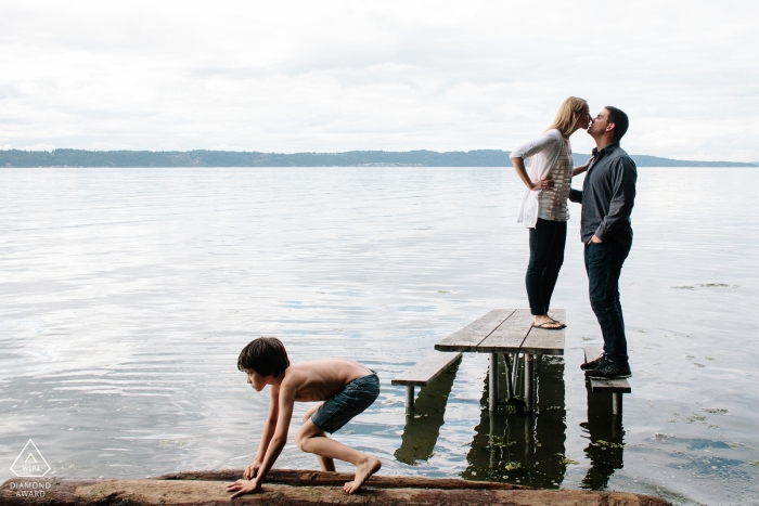 Photo by: <a href="https://www.wpja.com/photos/diamond-award-top-wedding-engagement-photographer/2427006">Ron Storer - Auburn Washington Creative Engagement Session Puget Sound - Couple kissing on picnic table in water