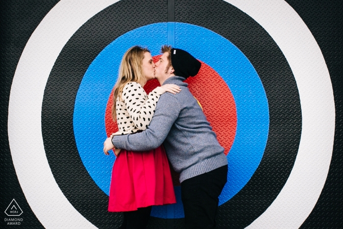 Photo by: <a href="https://www.wpja.com/photos/diamond-award-top-wedding-engagement-photographer/2427021">Ron Storer - Auburn Washington Creative Engagement Session Puget Sound - Couple kissing in front of large colored target