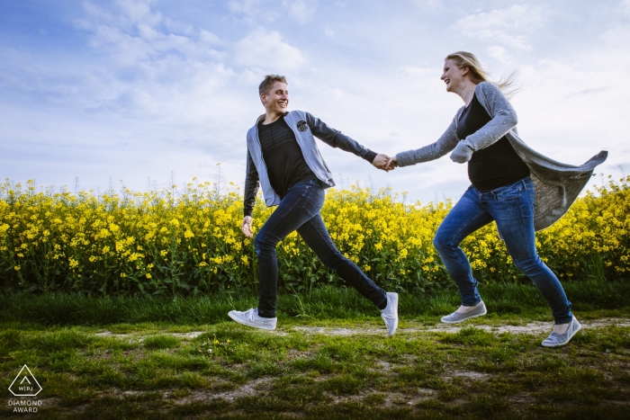 Photo by: <a href="https://www.wpja.com/photos/diamond-award-top-wedding-engagement-photographer/2455951">Rosa Engel - Aachen Nordrhein-Westfalen Engagement shoot in Aachen of a couple running through a field of yellow flowers.