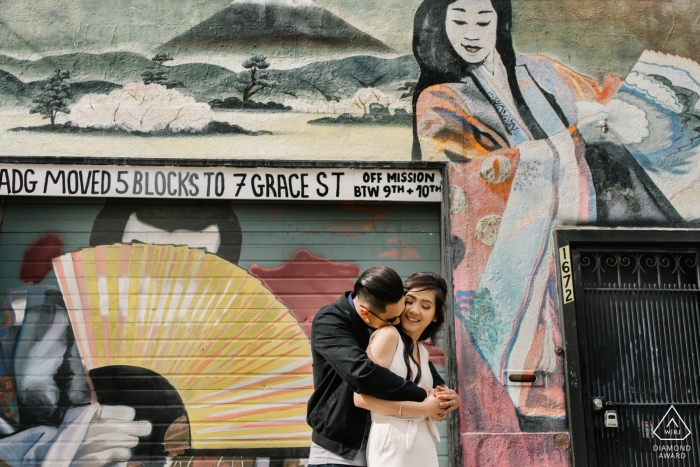 Sessão de fotos de noivado de um casal de pé juntos na frente de um mural em San Francisco.