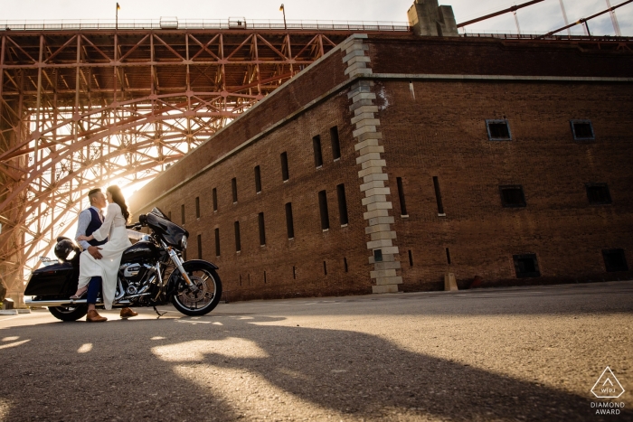 Verlobungsfotosession eines jungen Paares, das auf einem Motorrad vor einem Backsteingebäude in San Francisco sitzt.