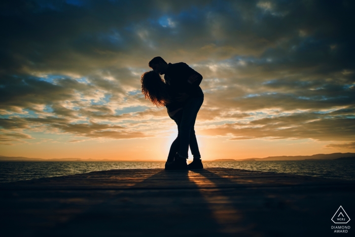 Photo de fiançailles d'un couple s'embrassant et se profilant au coucher du soleil au lac Trasimeno, en Italie.