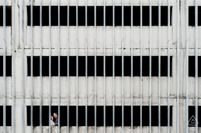 Photo by: <a href="https://www.wpja.com/photos/diamond-award-top-wedding-engagement-photographer/2457021">Franck Petit - Serignac sur Garonne Engagement photo of a couple standing in a white building with large, vertical beams in Agen, France.