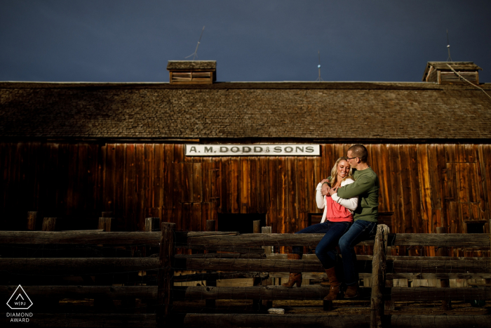 Foto di: <a href="https://www.wpja.com/photos/diamond-award-top-wedding-engagement-photographer/2457566"> Justin Edmonds - Denver Colorado Dodd Lake Engagement Spara con una coppia che si abbraccia su una recinzione durante la loro sessione di fidanzamento in granaio rustico in Colorado