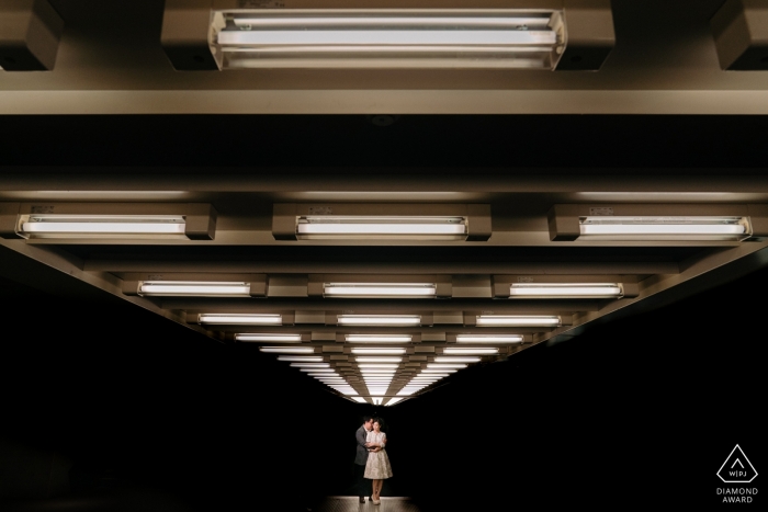 Foto de compromiso de una pareja en la distancia iluminada desde arriba en Amberes.