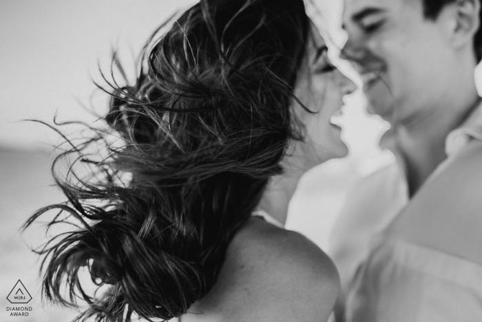 Black and white engagement portrait with wind blowing through the bride's hair in Plataforma de Osório.