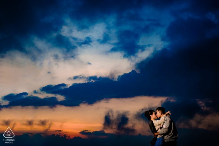 Photo by: <a href="https://www.wpja.com/photos/diamond-award-top-wedding-engagement-photographer/2463381">Vu Nguyen - Ho Chi Minh Engagement photoshoot of a couple kissing at dusk beneath blue clouds in Dalat.