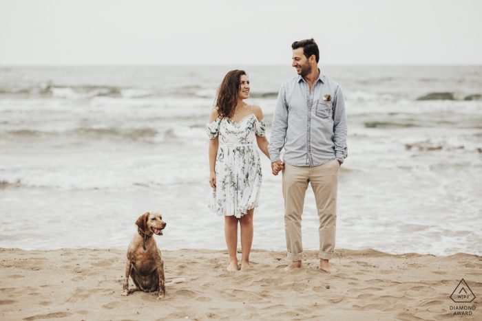 Pre-wedding photoshoot of a couple holding hands on the beach as their dog sits in front of them in Kocaeli, Turkey.