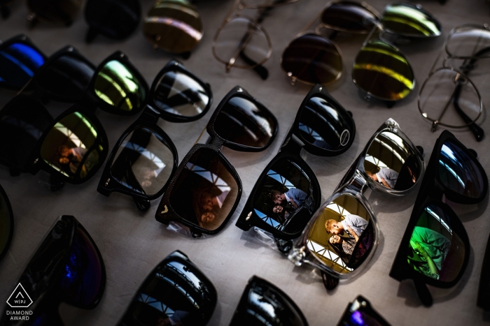 Photo by: <a href="https://www.wpja.com/photos/diamond-award-top-wedding-engagement-photographer/2463866">Pasquale Minniti - Reggio Calabria Engagement photo of a couple reflected in lenses at a sunglasses stand in Reggio Calabria.
