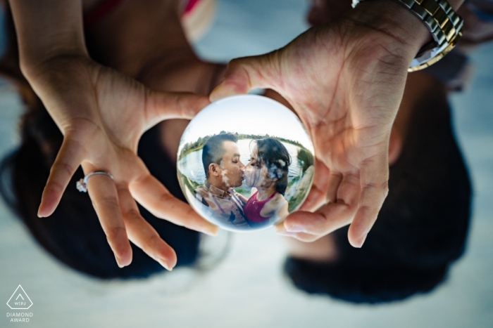 Portrait de fiançailles d'un couple s'embrassant se reflétant dans une boule de verre qu'ils tiennent ensemble à El Monte, Californie.