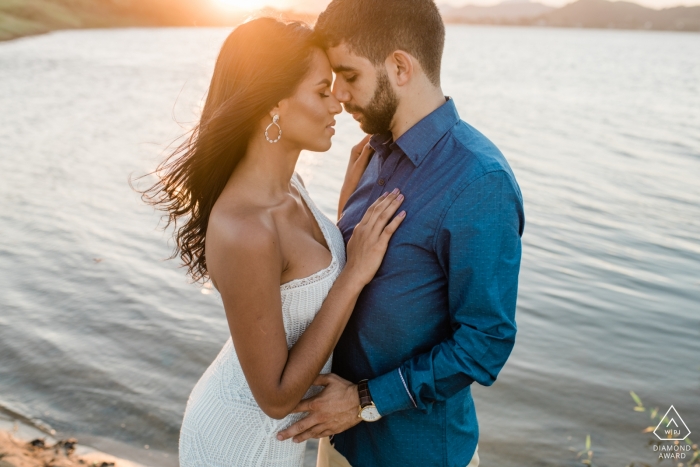 Macae engagement photography session captures the couple embracing in front of a pond while the sun sets behind them