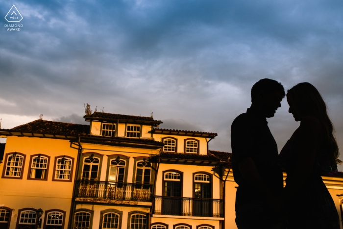 Photo by: <a href="https://www.wpja.com/photos/diamond-award-top-wedding-engagement-photographer/2466621">Vinicius Terror - Ouro Preto Minas Gerais The silhouettes of the couple are captured against a large golden yellow building in this Ouro Preto engagement photo session