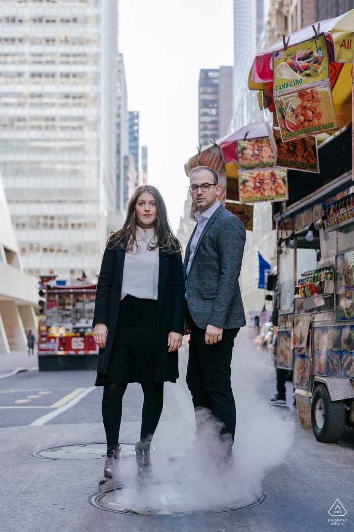 Photo by: <a href="https://www.wpja.com/photos/diamond-award-top-wedding-engagement-photographer/2467136">Chloe Delmonte - London London A couple stands on a steaming manhole cover on a crowded city street in this New York City engagement portrait session