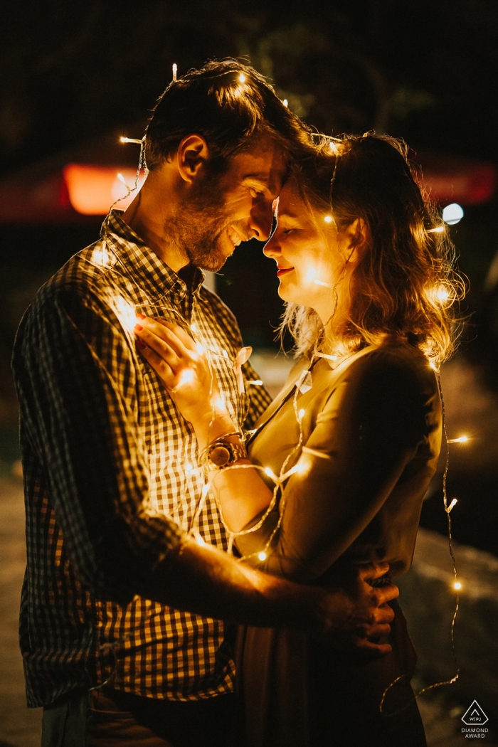 Topoľčany, Slovakia - couple drapes themselves in strands of lights while embracing for their engagement photoshoot