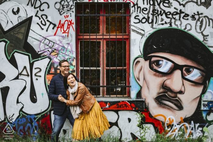 Engagement portrait shoot captured couple laughing in front of a serious looking gravity man as captured in Ljubljana