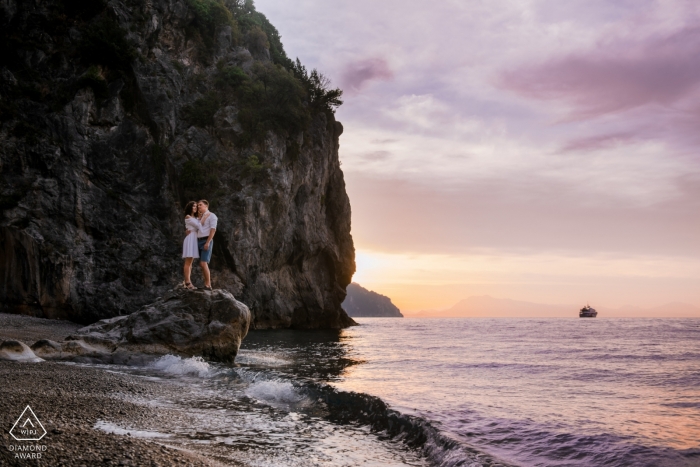 Amalfi, Italien – Bei diesem Verlobungsporträtshooting steht ein Paar auf einem Felsbrocken, während die Sonne über dem Meer untergeht