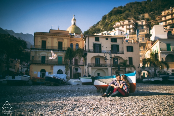 La séance photo de fiançailles de Salerno capture le couple assis par terre à côté d'un bateau à rames à rayures rouges