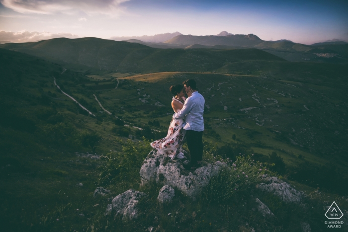 Diese Verlobungsfotosession in den Abruzzen und Italien zeigt das Paar, wie es hoch oben auf einem grasbewachsenen Hügel steht, während in der Ferne dunstige Berge aufragen