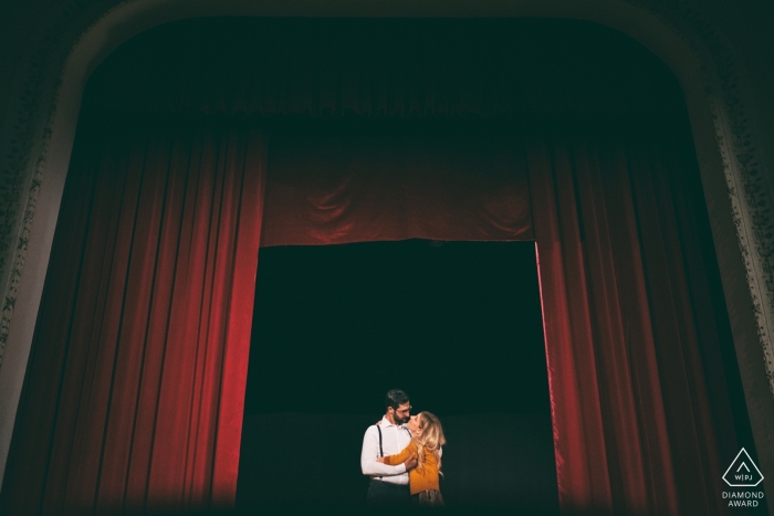 Esta imagen de una pareja que se besa en una abertura en un telón rojo fue capturada durante esta sesión de fotos de compromiso de Lazio