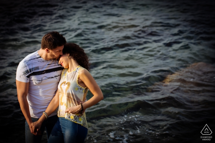 Photo by: <a href="https://www.wpja.com/photos/diamond-award-top-wedding-engagement-photographer/2472951">Danilo Muratore - Rosarno Reggio Calabria Calabria - the happy couple poses in front of choppy water in this engagement shoot