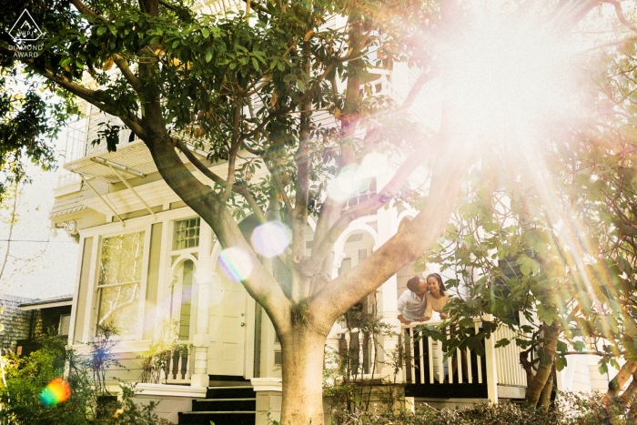 Cette image d'un couple s'embrassant sur le porche pendant que le soleil brille à travers les arbres a été capturée lors d'une séance photo d'engagement à San Francisco