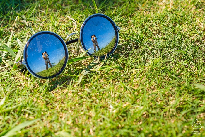 Fuijan - we can see the reflection of the couple kissing in a pair of glasses resting on the grass in this pre-wedding portrait session 