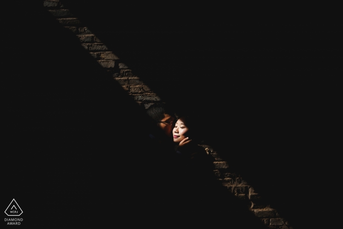 Photo by: <a href="https://www.wpja.com/photos/diamond-award-top-wedding-engagement-photographer/2475386">Qi Xiang - Nanping Fuijan - we get just a small glimpse of the couple in a sliver of light as they pose for their pre-wedding portraits in an old warehouse