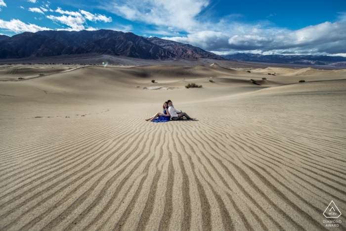 Ein Paar sitzt Rücken an Rücken inmitten einer bergigen Wüste in diesem Verlobungsporträt-Shooting im Death Valley