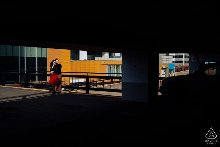 Verlobungsfotosession in Edmonton, AB – Paar lächelt in der Sonne vor einem mehrstöckigen Parkhaus