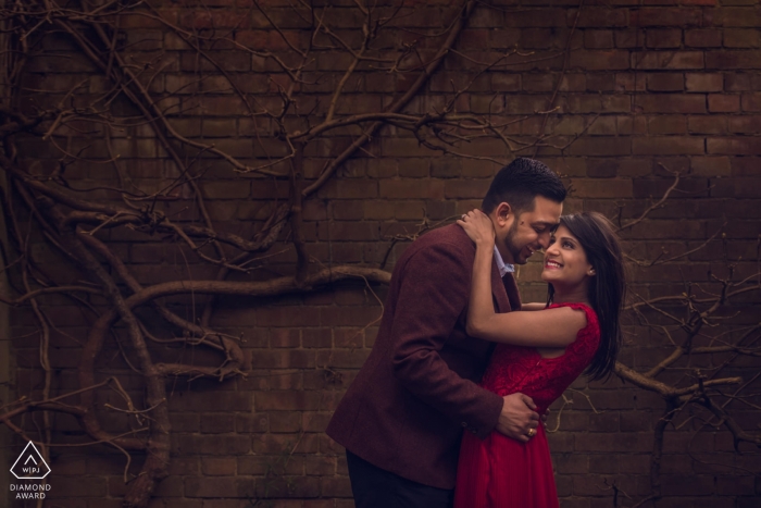 Photo by: <a href="https://www.wpja.com/photos/diamond-award-top-wedding-engagement-photographer/2476521">Jay Hoque - Uxbridge London London, UK engagement PhotoShoot- couple smile happily at each other in front of a vine covered brick wall
