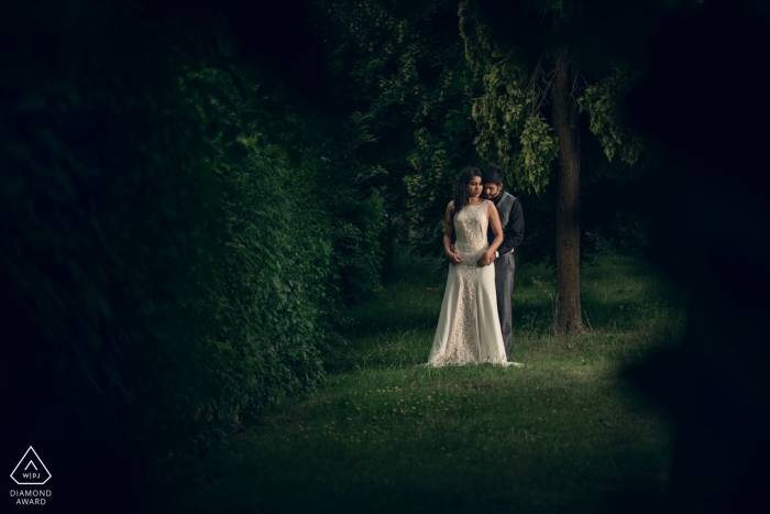 Bath, UK engagement portrait shoot- man gives his future bride a hug from behind as they stand in a lush green forest