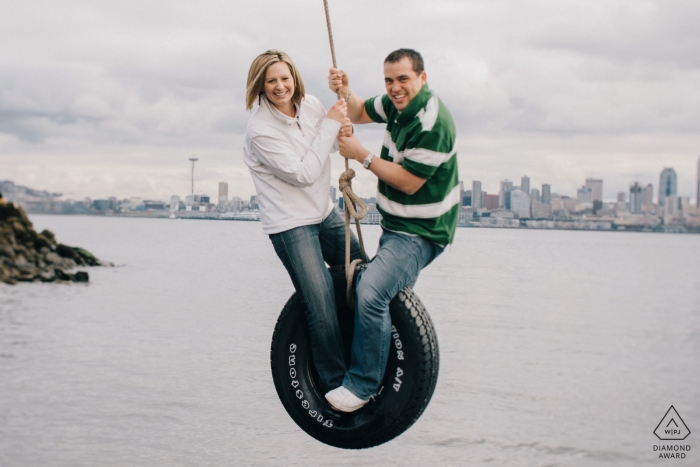 Photo de fiançailles de West Seattle, Washington, avec un couple balançant un pneu temporaire au-dessus de Puget Sound