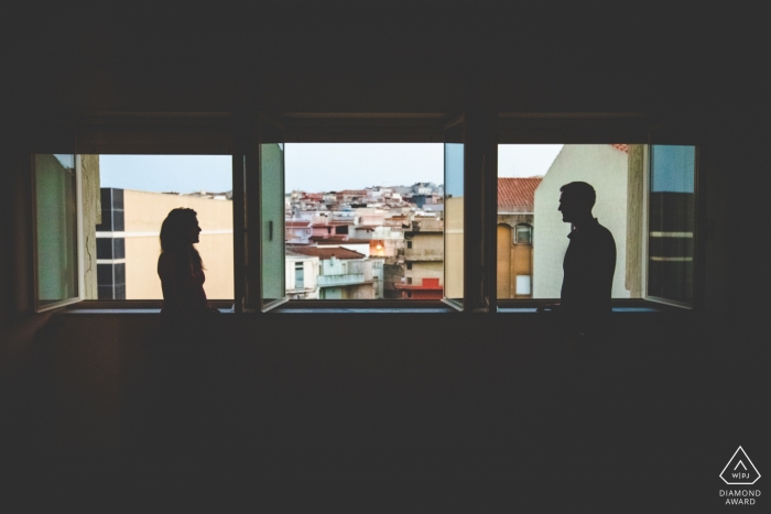 Ein Mann und eine Frau werden durch die Fenster in ihrem Haus in Pachino in diesem Verlobungsfoto von einem Fotografen aus Syrakus, Sizilien silhouettiert.