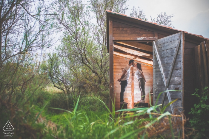 The bride stand on crates and kiss in a small hut during their Priolo engagement photoshoot by a Sicily photographer.