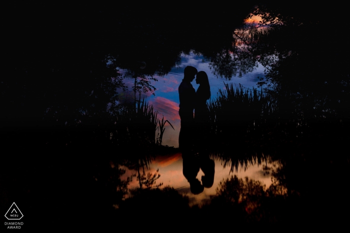 The bride and groom's silhouettes are reflected in a pond in during this London, evening engagement shoot by an England photographer.