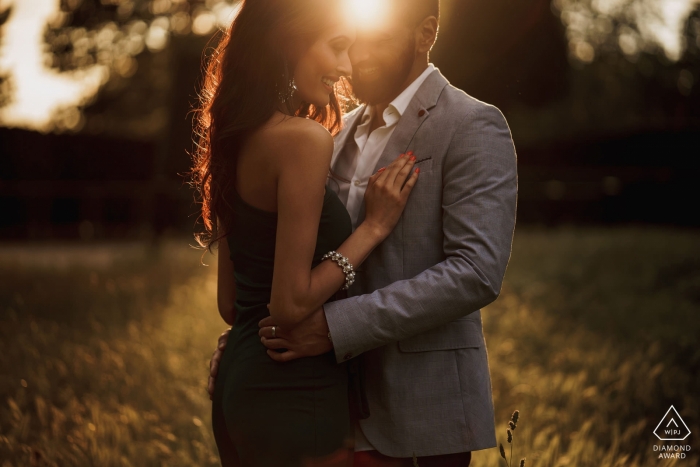 A couple stands together in a field with the sun shining between them in this pre-wedding photo by a London, England photographer.