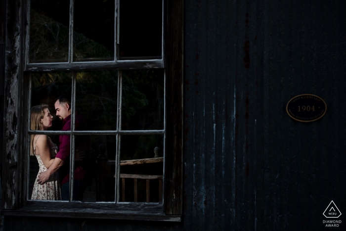 A man and woman can be seen holding one another through a window during their engagement session in Fort Myers by a Key West, FL photographer.