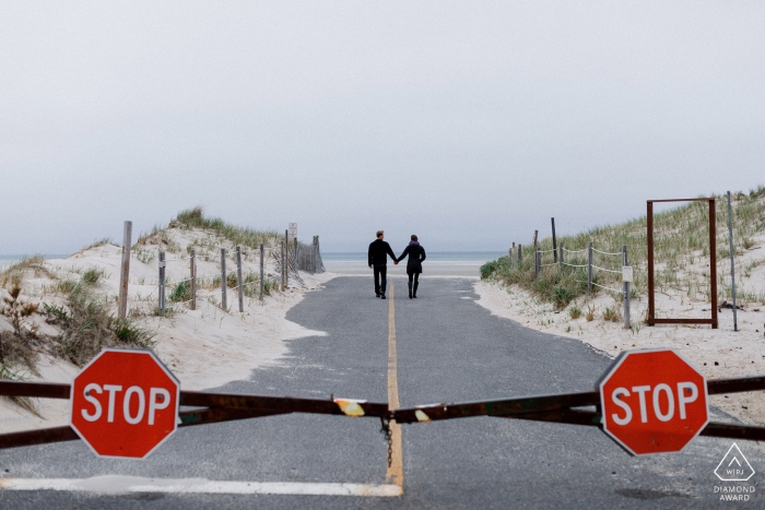 Photo by: <a href="https://www.wpja.com/photos/diamond-award-top-wedding-engagement-photographer/2483366">Alex Paul - Boston Massachusetts A couple walks hand in hand down the road with two stop signs behind them in Cape Cod in this engagement photo by a Boston, MA photographer, who is also available for RI, VT, NH and CT weddings.