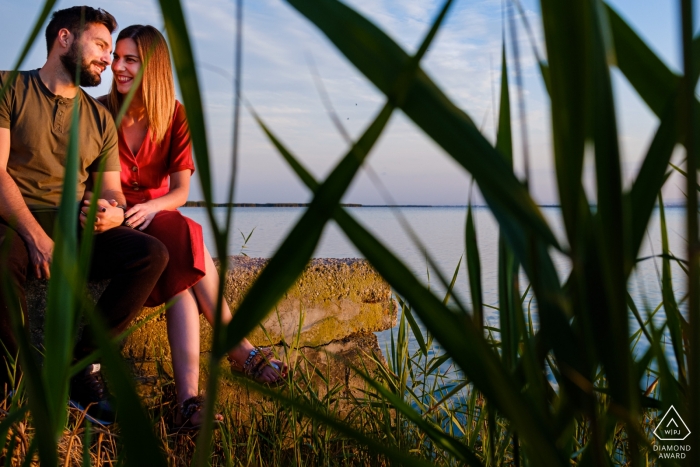 O casal senta-se em uma pedra junto à água nesta foto pré-casamento por um fotógrafo de Alicante, Valência.